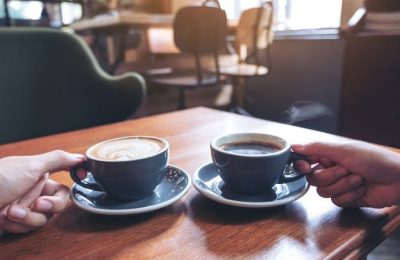 Closeup-imagem-das-maos-de-duas-pessoas-segurando-cafe-e-copos-de-chocolate-quente-na-mesa-de-madeira-no-cafe-_-Foto-Premium